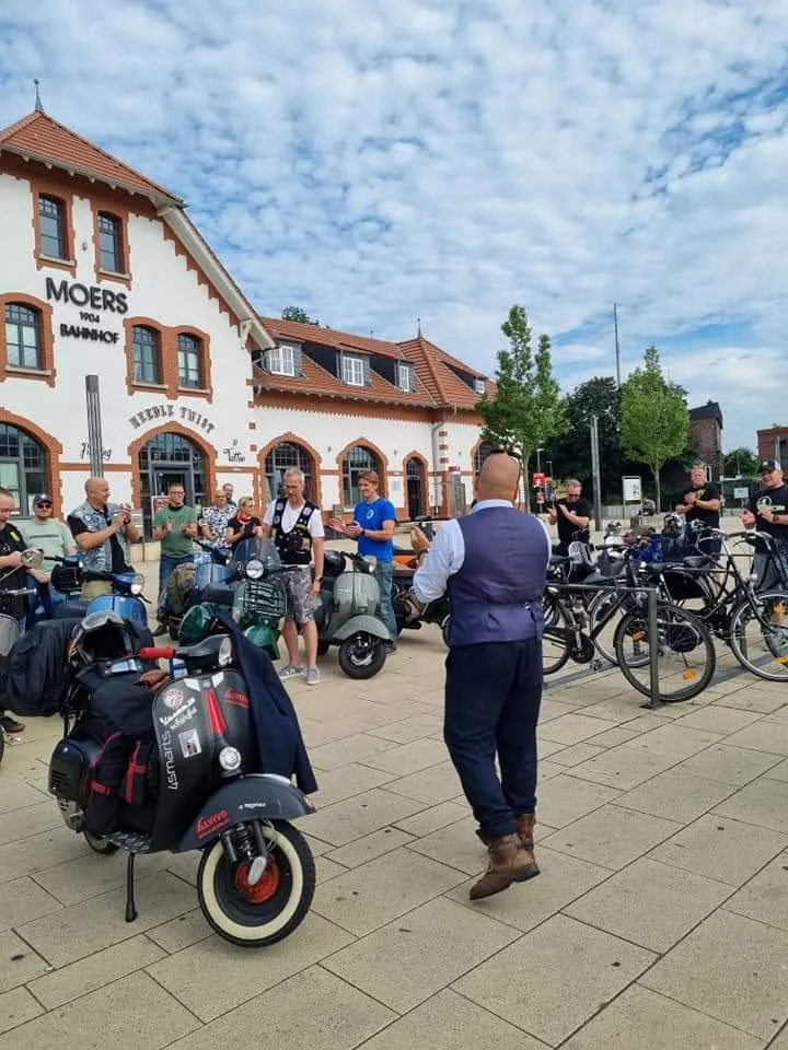Markus André Mayer in suit addressing Vespa club crowd at Moers Bahnhof during Gentleman Giro 2021