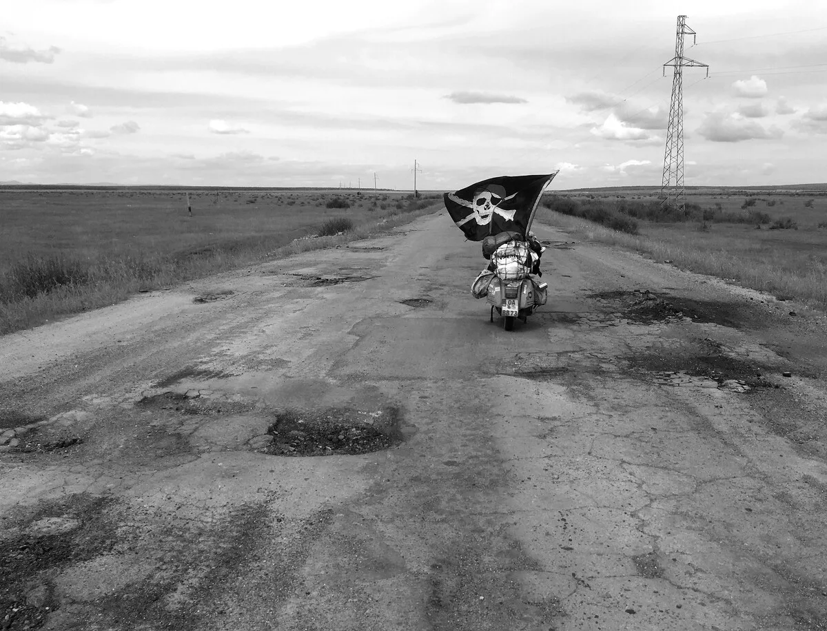 Markus André Mayer Vespa with pirate flag on broken road Kazakhstan steppe — 2018 world circumnavigation