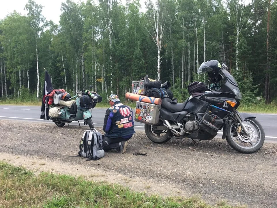 Vespa next to a large touring motorcycle on a Siberian roadside — size comparison during 2018 world circumnavigation