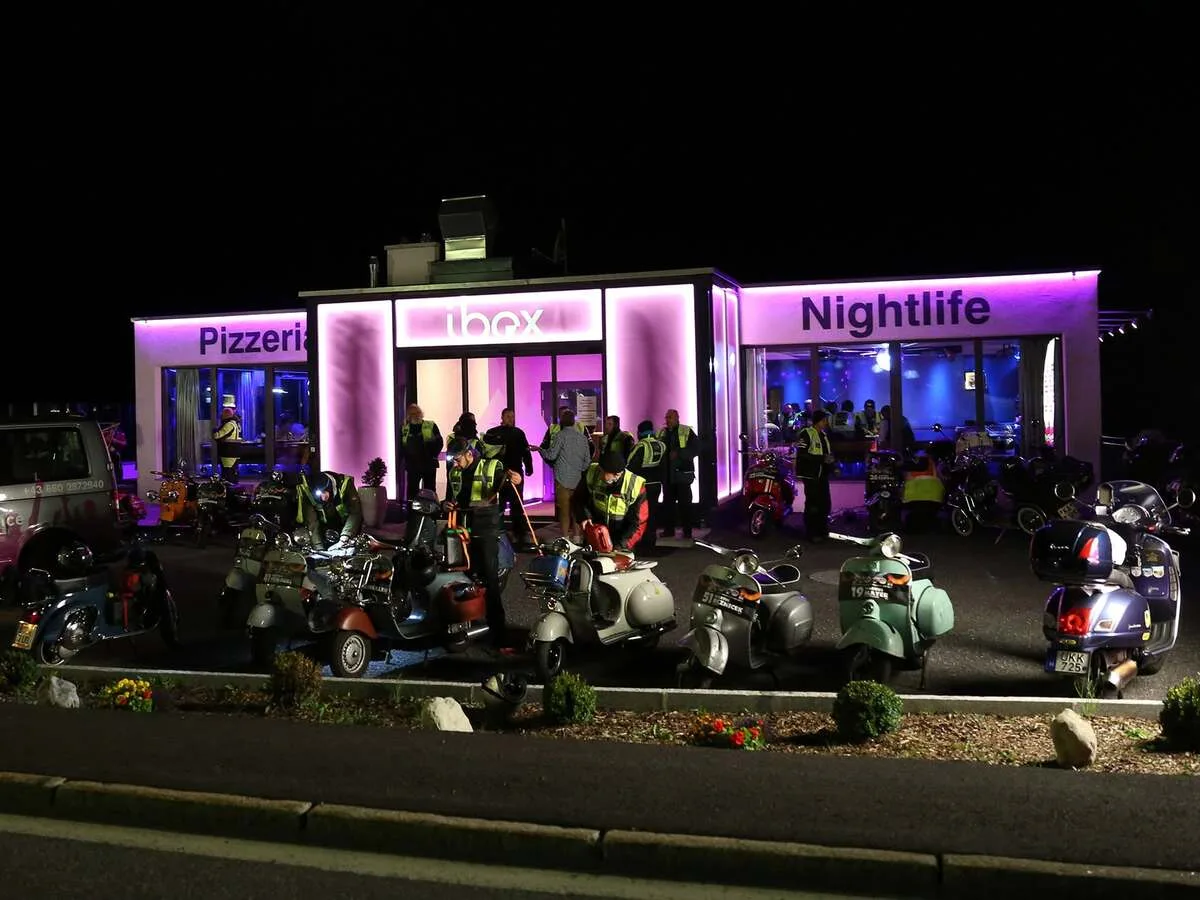 Around 55 Vespas parked outside Ibex Pizzeria at night during a warm stop on the PreRe II 2015 Vespa night rally Austria